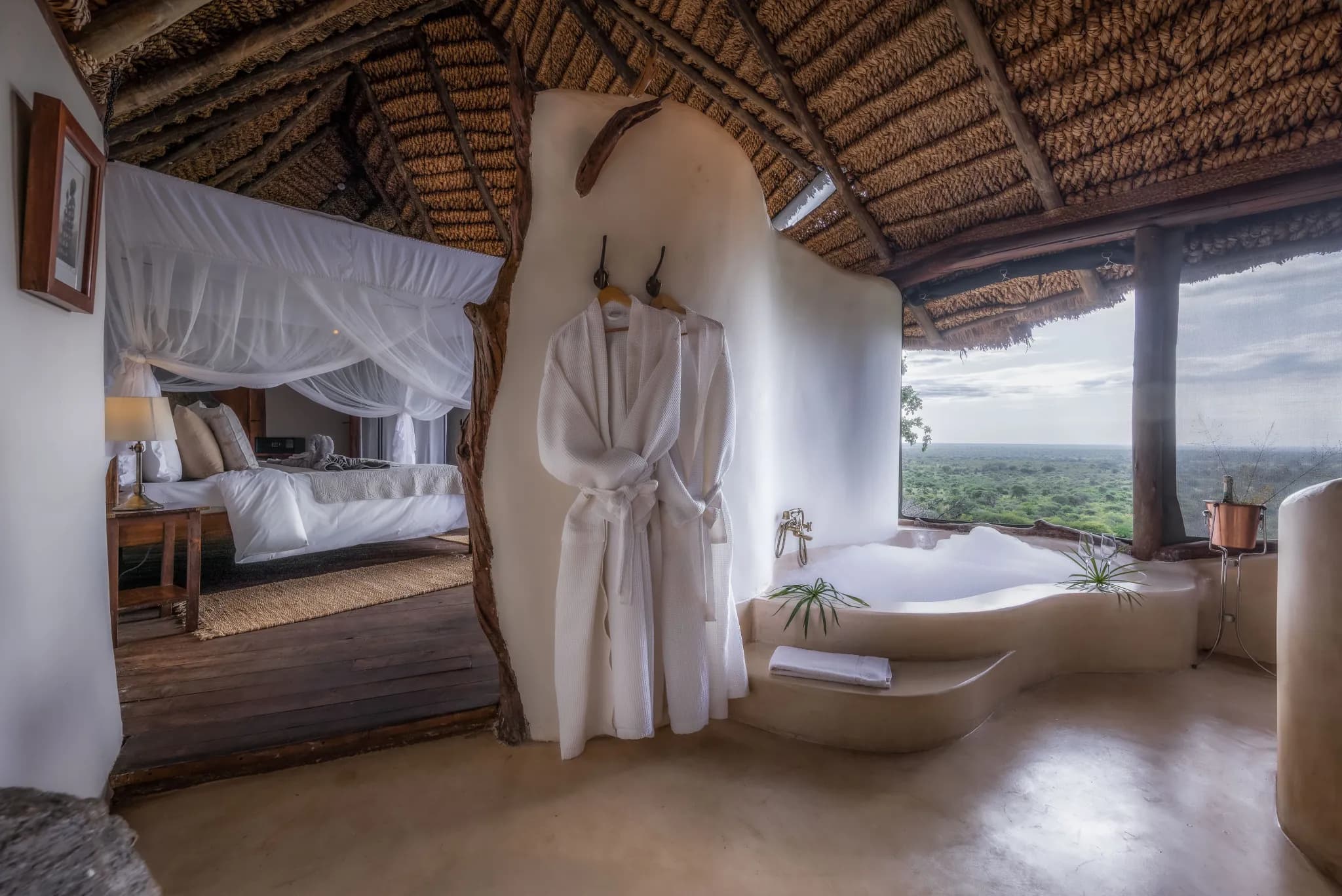 A Honeymoon Suite at Elsa's Kopje, the open-air bathtub framing the plains through a wide window — Photo: Elewana Collection