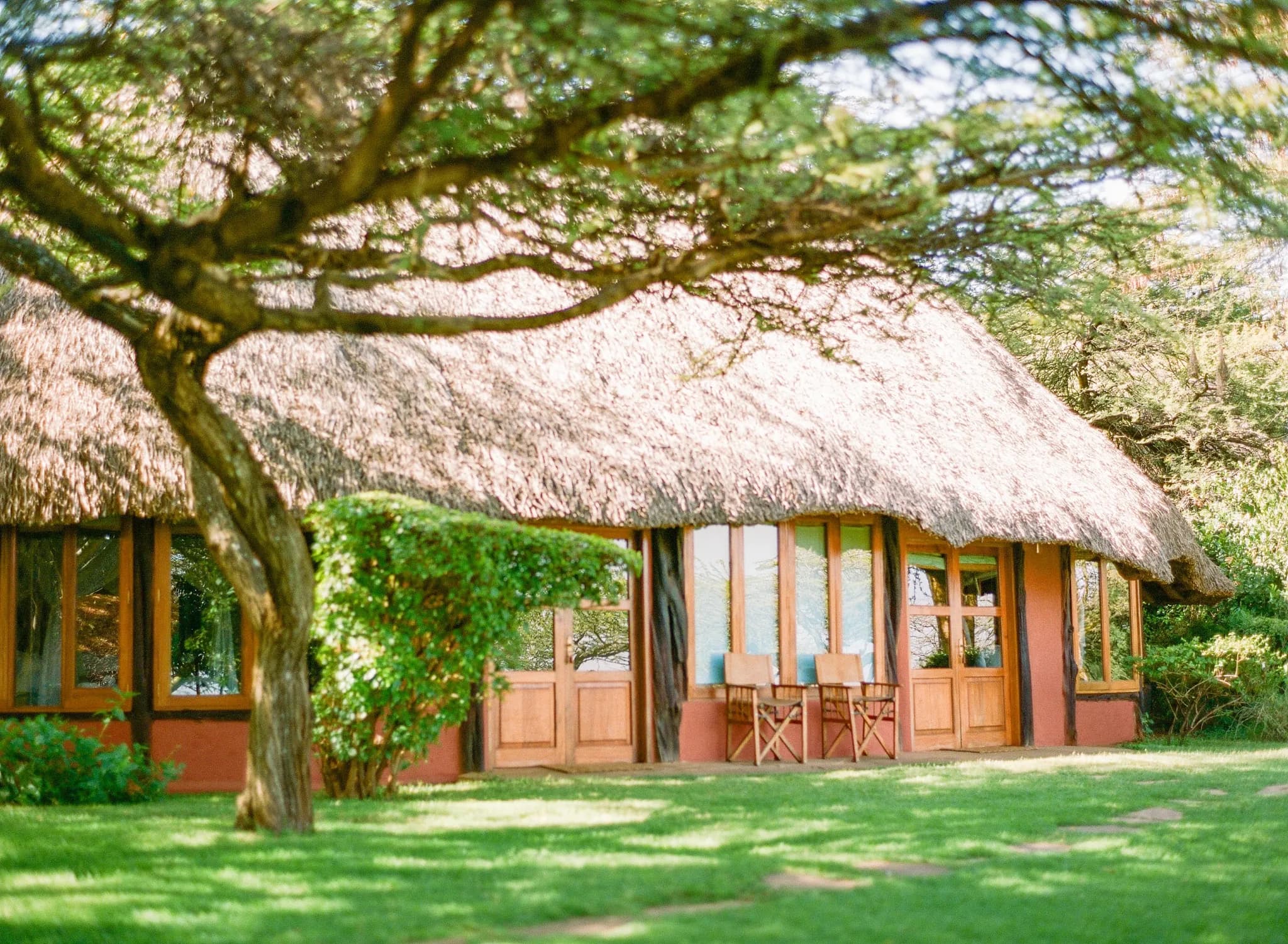 A thatched cottage on the manicured lawns at Kifaru House — Photo: Elewana Collection / Oliver Fly Photography