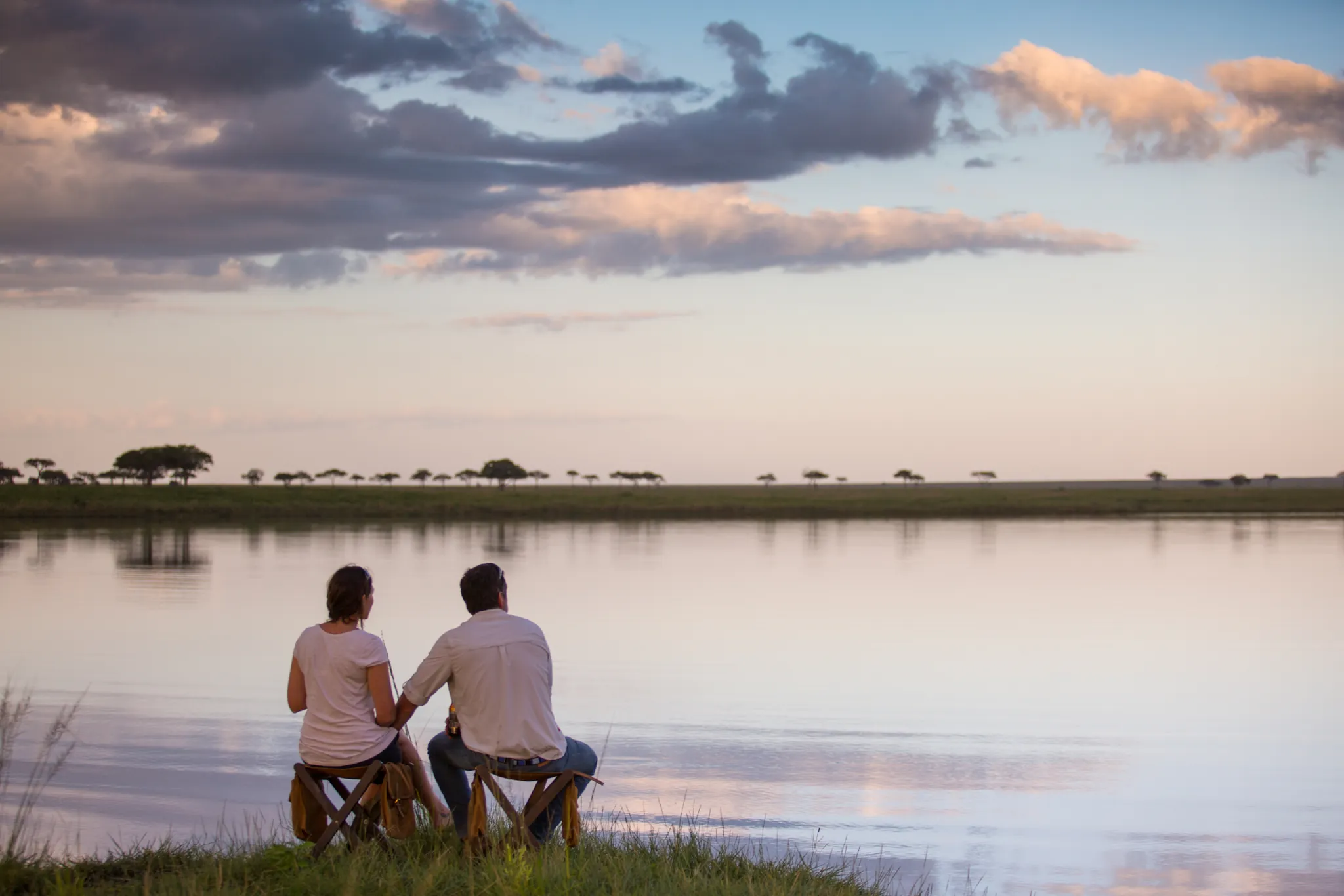 A couple at a Lake Magadi sundowner near Serengeti Pioneer Camp, the plains dissolving into dusk — Photo: Elewana Collection
